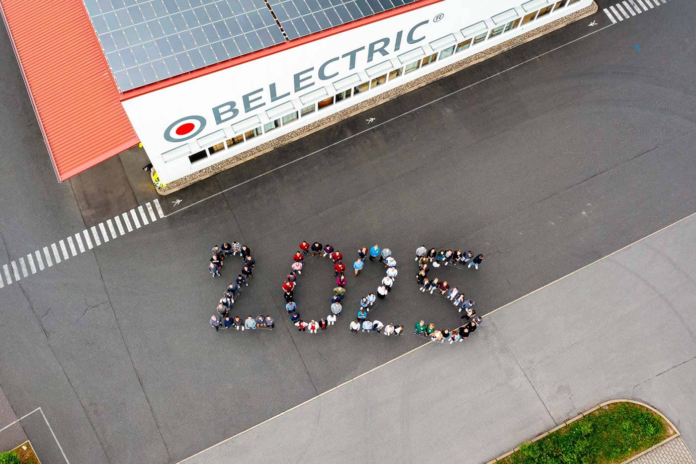 Drohnenaufnahme: BELECTRIC-Mitarbeitende formieren auf einem Parkplatz gemeinsam die Zahl 2025