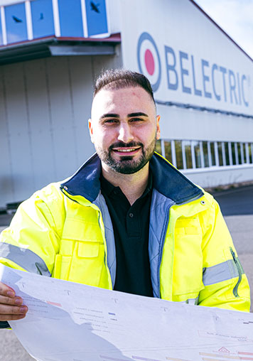 A BELECTRIC employee working in Engineering holds a plan and smiles into the camera