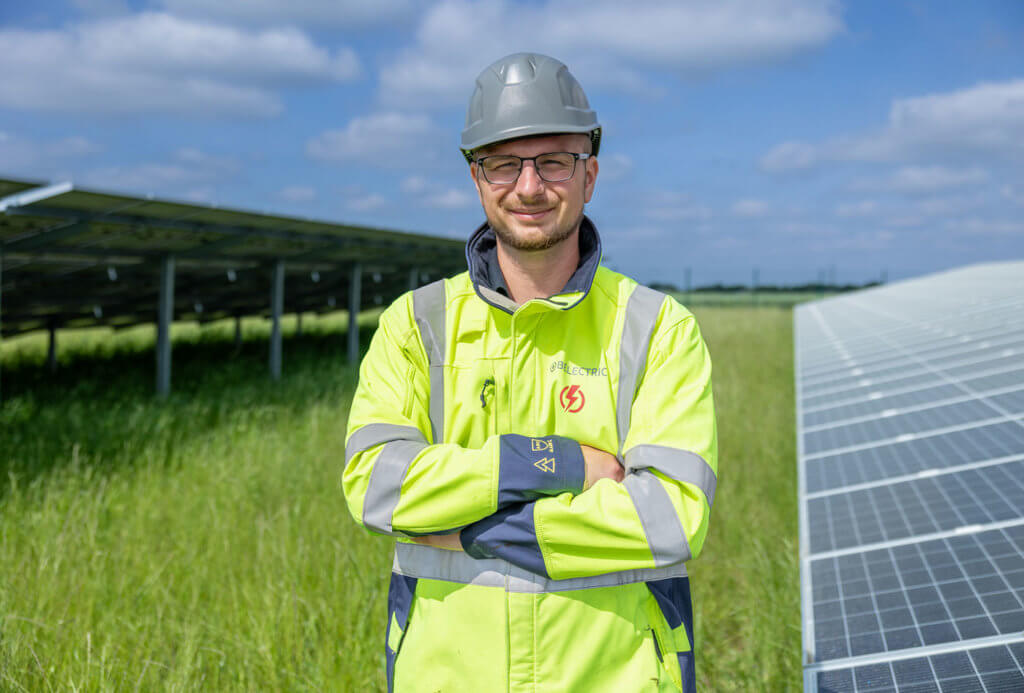 An electrician stands in front of a solar farm 