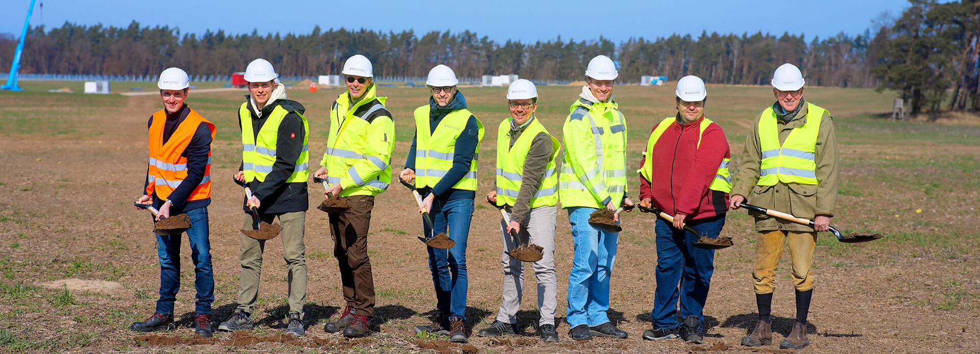 Eight people wearing high-visibility jackets stand on the construction site of the solar farm Borrentin and hold spades in their hands