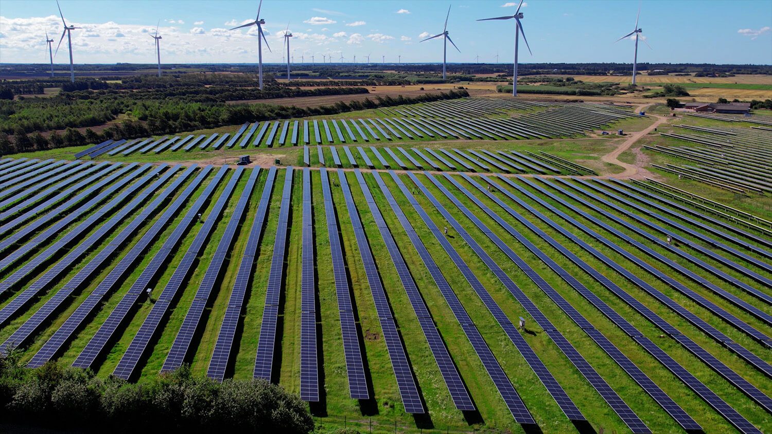 solar farm seen from above with green fields and wind turbines in the background