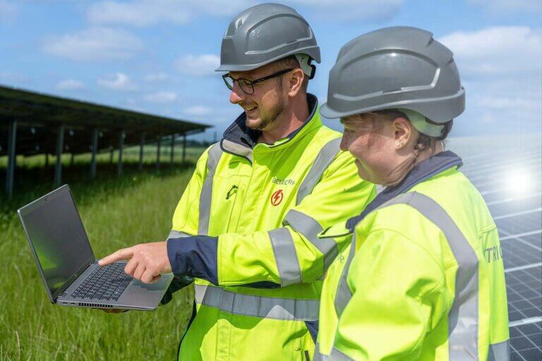 An electrician on a solar farms shows a second, younger electrician something on a laptop screen