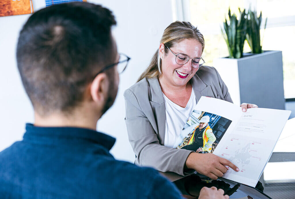 A woman holds a brochure and points to something written inside it. She smiles.