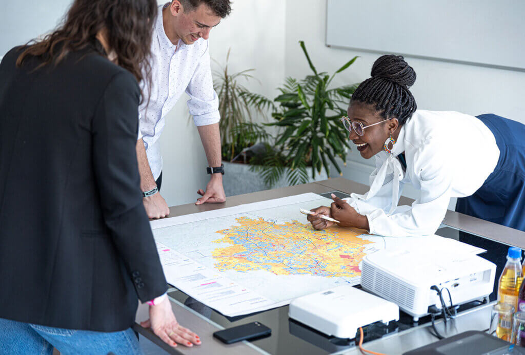 Three employees stand around a meeting table. One of them looks at the other two and laughs.