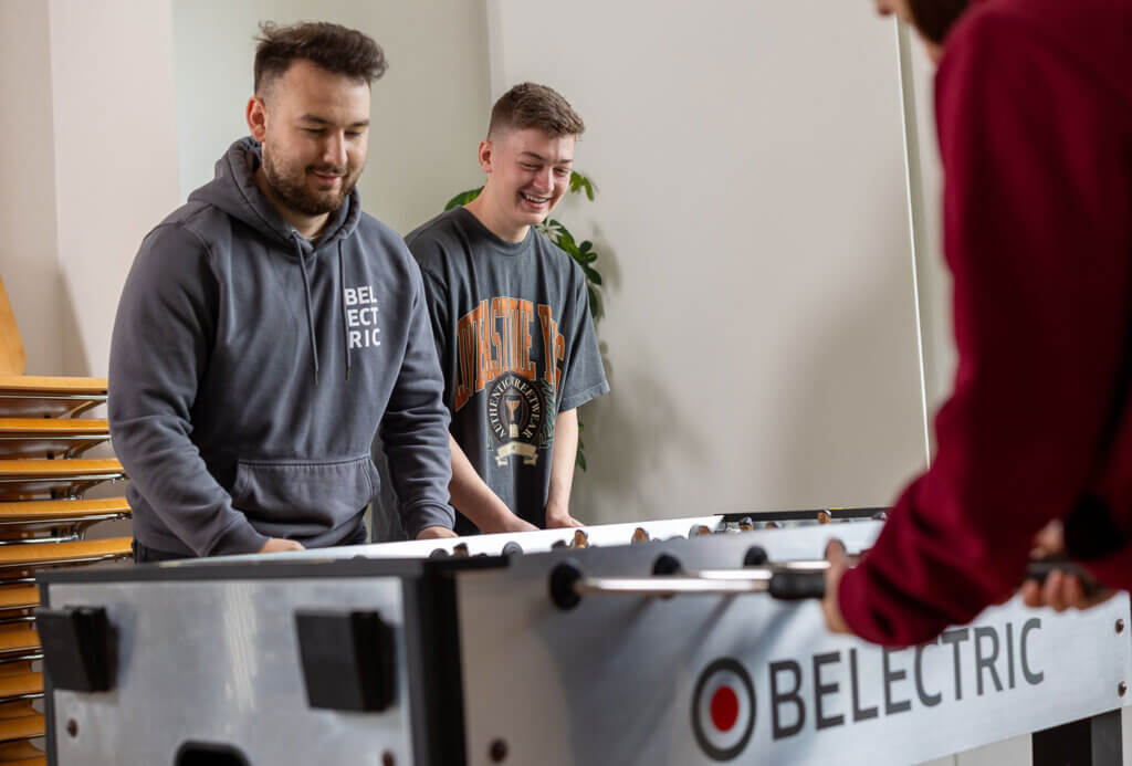 Two male trainees play table football and laugh.