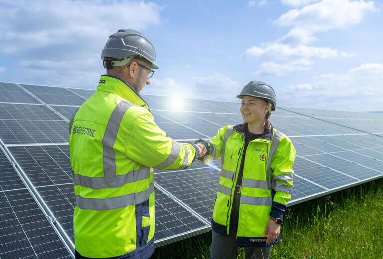 Two electricians who pursue a career at solar company BELECTRIC fist-bump in front of a solar power plant.