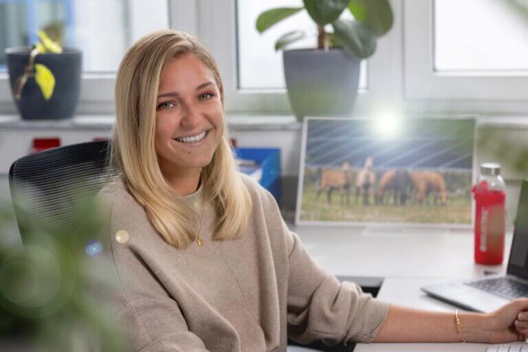 An office administration trainee sits in front of a desk and smiles into the camera.