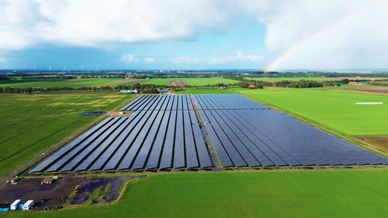 solar farm constructed by BELECTRIC Netherlands with a rainbow and wind turbines in the background