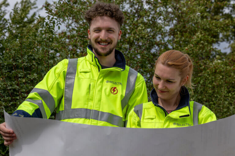 two employees in work clothes standing in front of trees and looking