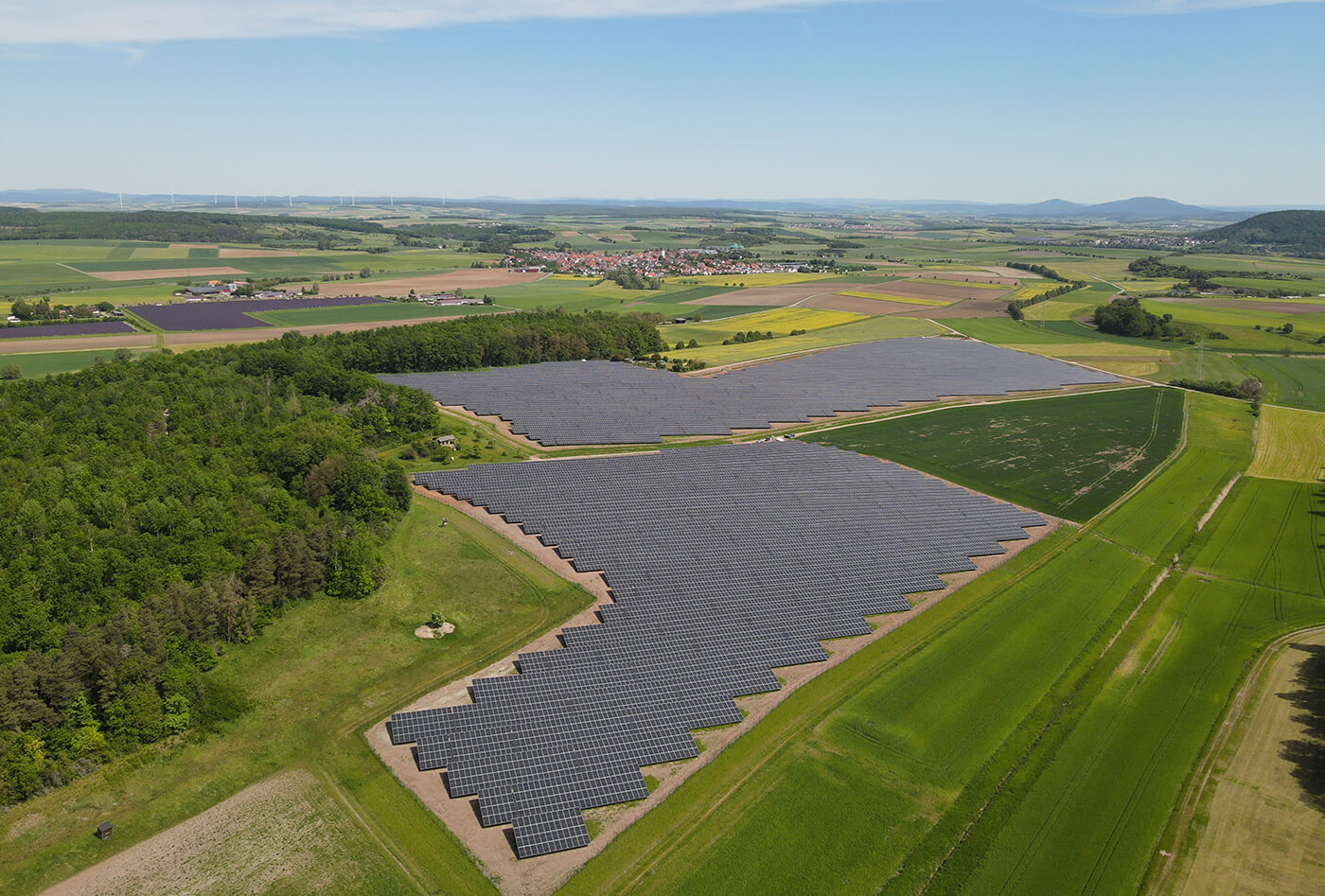 Showing a solar park with wind turbines in the back.