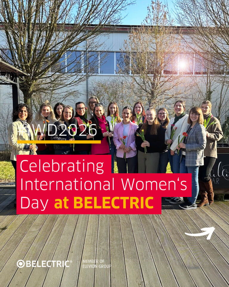 Female BELECTRIC employees stand together holding flowers. The text reads "Celebrating International Women's Day at BELECTRIC".