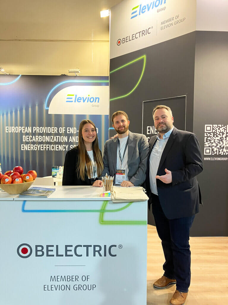 Three BELECTRIC employees standing in front of a trade fair booth.
