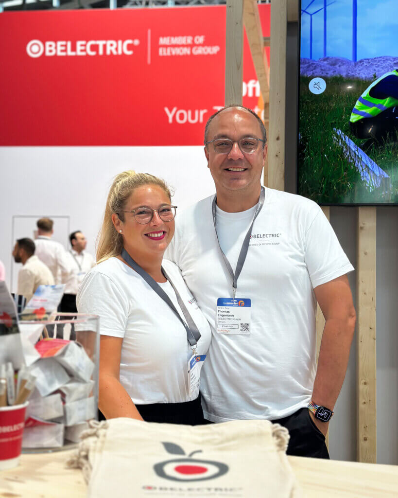 Zwei BELECTRIC-Mitarbeitende stehen hinter einem Tresen auf der Intersolar und lächeln in die Kamera.