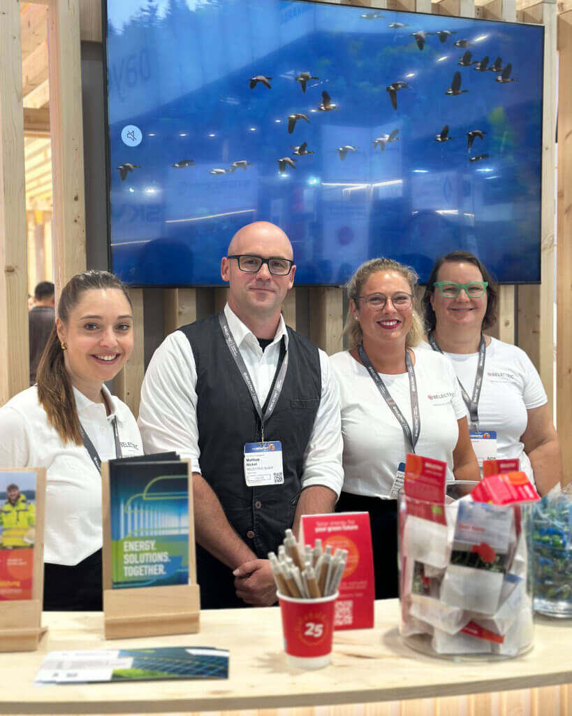 Vier BELECTRIC-Mitarbeitende stehen hinter einem Tresen auf der Intersolar und lächeln in die Kamera.