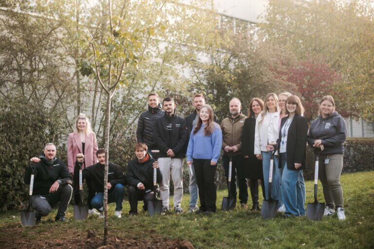 Mehrere BELECTRIC-Mitarbeitende stehen um einen jungen, frisch gepflanzten Baum